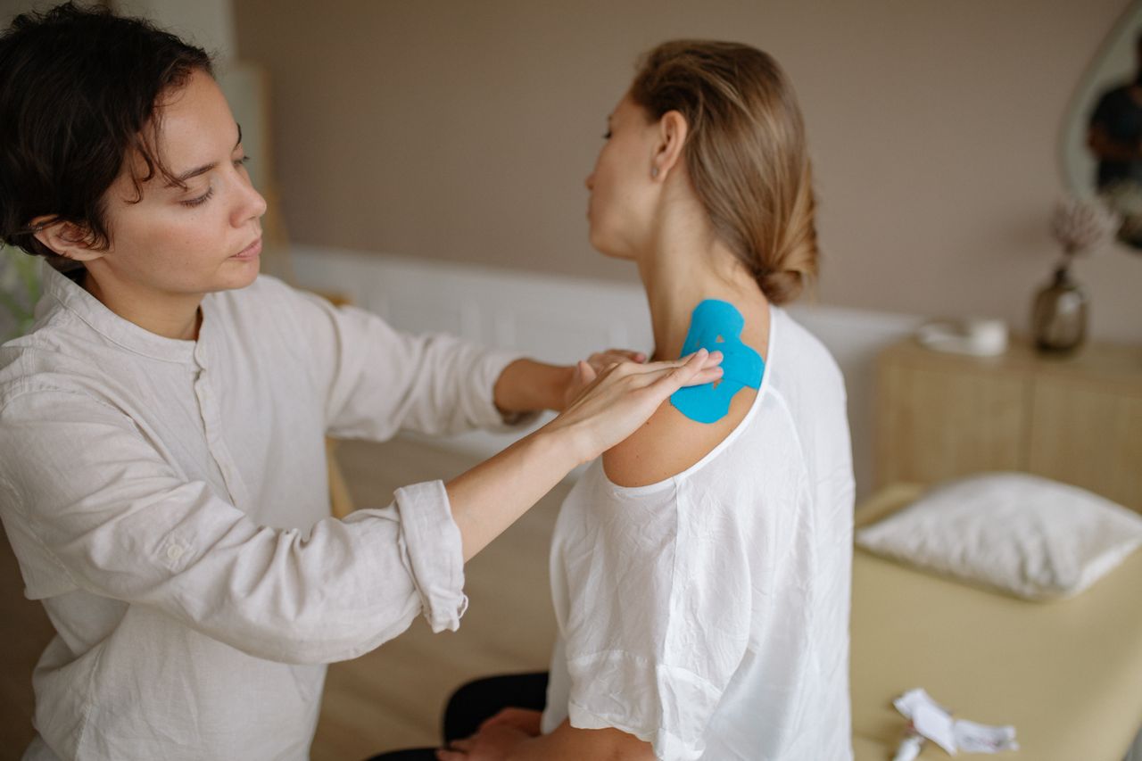 Healthcare professional applying therapeutic kinesiology tape on patient shoulder for support